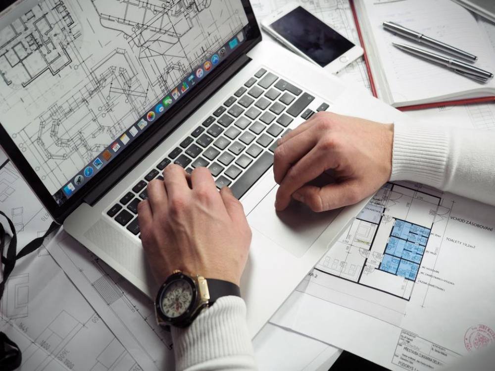 Mains sur le clavier d'un ordinateur portable, posé sur des plans techniques