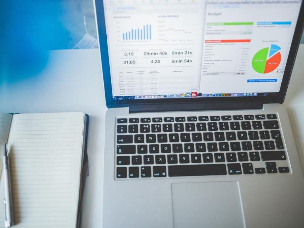 Tableau de bord de gestion affiché sur un ordinateur portable, à côté d'un carnet